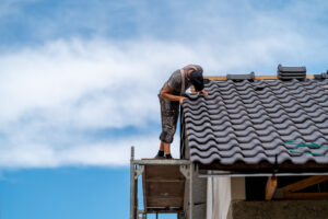 Home craftsman on scaffolding installs ceramic tile on the roof of a family home, copy space